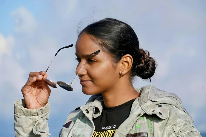 Young woman holding sunglasses with sky background